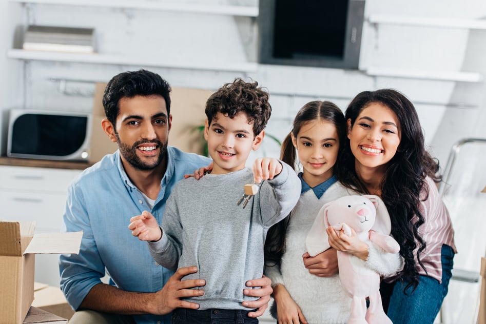 Cheerful latin kid holding keys from new home near happy hicpanic family