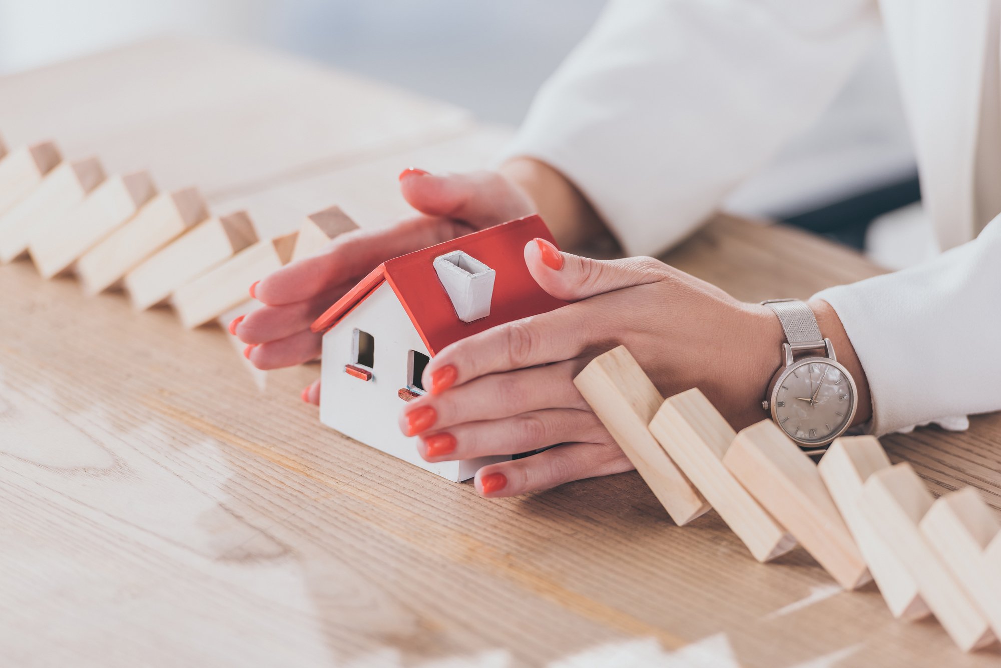 Cropped view of risk manager protecting house model from falling wooden blocks with hands