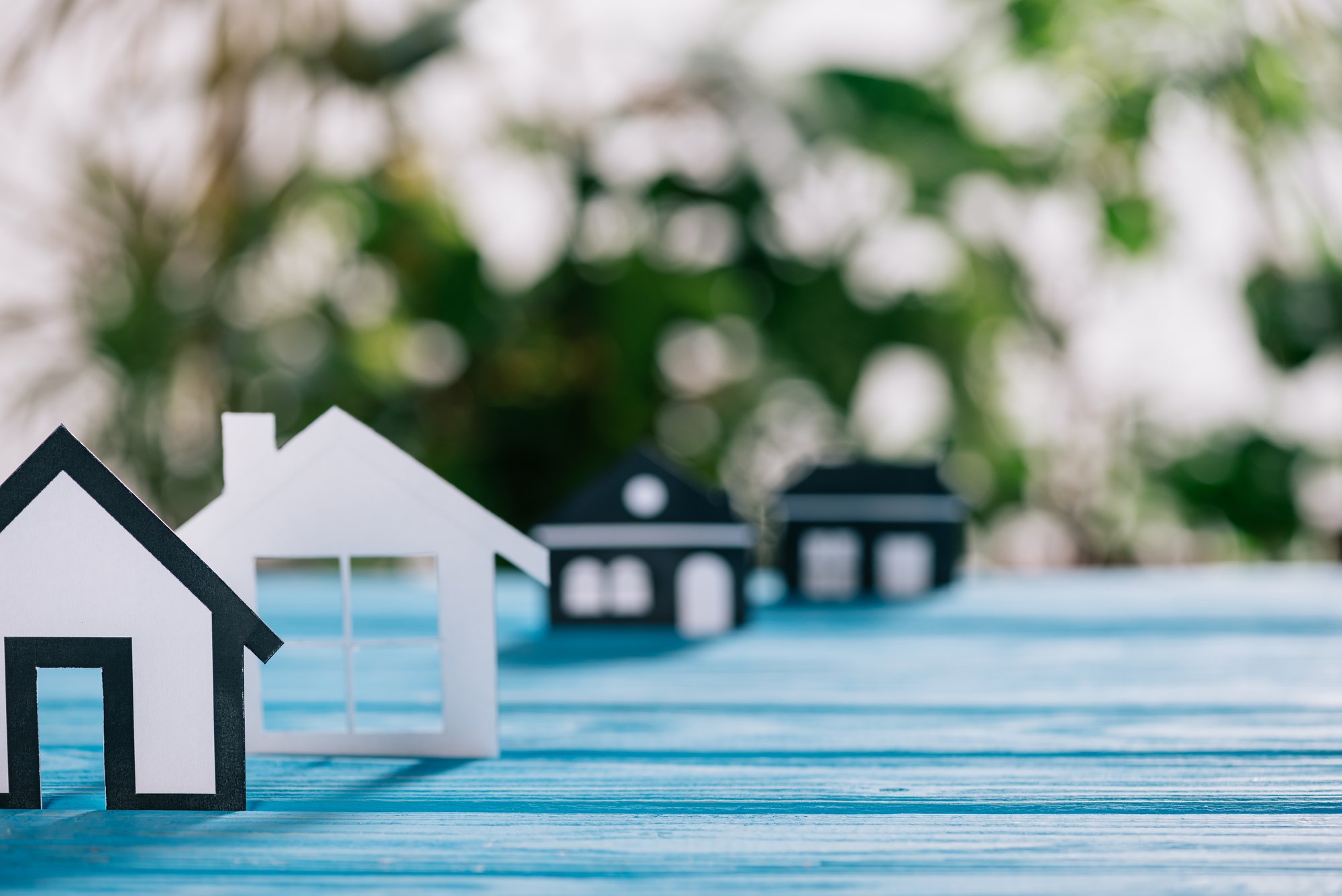 Selective focus of black and white paper houses on blue wooden desk, mortgage concept