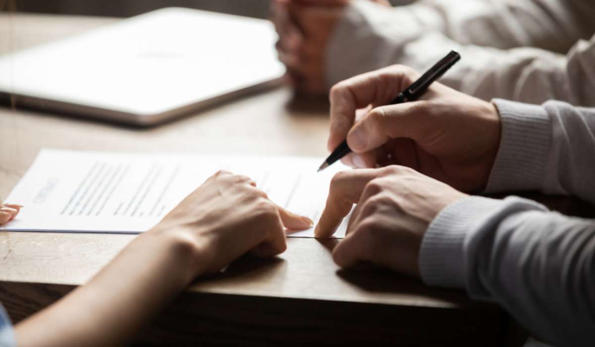 Solicitor pointing at insurance contract showing male client where to write signature sign sale