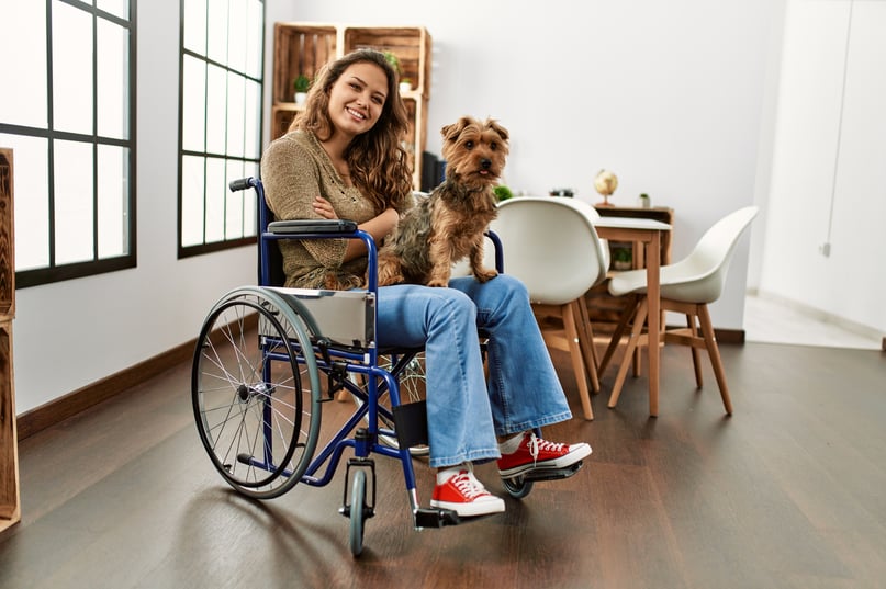 Young hispanic girl sitting on wheelchair at home smiling looking to the side and staring away thinking