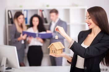 Female landlord holding a model home while her property management team works in the background