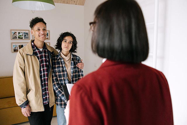 young-couple-speaking-with-a-woman-holding-a-clipboard-inside-a-home young-couple-speaking-with-a-woman-holding-a-clipboard-inside-a-home